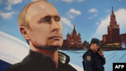 Розмова по телефону біля пропагандистського плакату з Володимиром Путіним в окупованому Донецьку у день російських місцевих виборів 2023 року