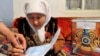 Женщине помогают поставить отметку в избирательном бюллетене в день голосования на досрочных выборах президента Казахстана. Алматинская область, 3 апреля 2011 года.