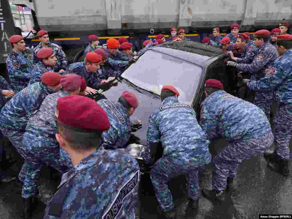Police try to remove a car that is preventing them from also removing a large truck that is blocking a road in Yerevan.