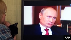  “Крым. Мекенге карай жол” деген тасмада сүйлөп жаткан Путинди көрүп отурган аял