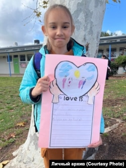 Алиса с поделкой из школы о том, что такое любовь. Первая строчка: "Любовь — это мои мамы", США