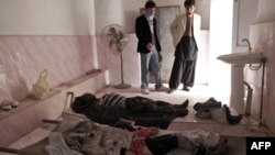The bodies of a girl and a boy who were killed in an acid attack are watched over by two men in a room in the main hospital of Ghazni city on March 30.