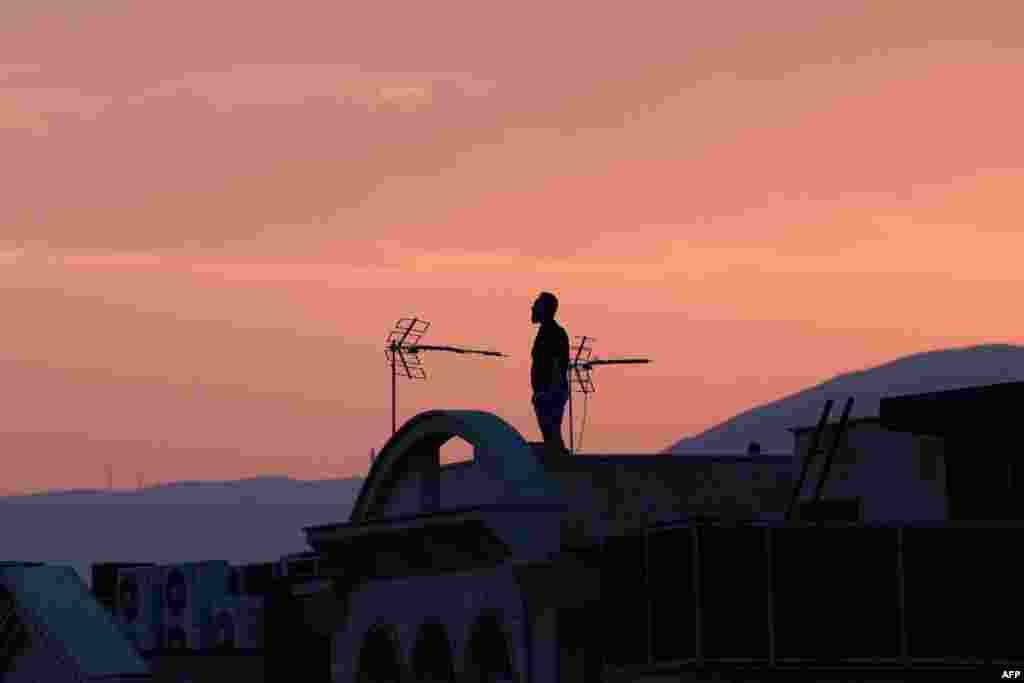 Тегерандагы имараттын үстүндө тынымсыз бомбалоо менен батып бараткан күндү карап турган эркек. 