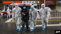 Медики в защитных костюмах и масках ведут пациента в клинику в городе Ухань. 26 января 2020 года.