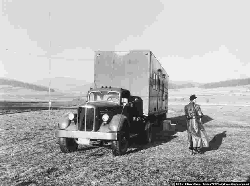 Вооруженный охранник патрулирует грузовик со средневолновым радиопередатчиком в Западной Германии, недалеко от границы с Чехословакией, в 1955 году.Поскольку коммунистические государства начали глушить передачи РСЕ и Радио Свобода, Радио Свободная Европа развернуло десятки мобильных передающих станций, таких как та, что изображена здесь, которые могли работать в непосредственной близи от "железного занавеса".