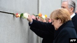 Меркел Берлин дубалынын урандысынын калдыгына роза гүлүн коюп жатат.