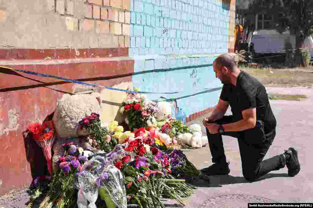 Чоловік став на коліно, віддаючи честь пам'яті загиблих через російську атаку людей у Києві. Їхня кількість, за останніми даними, зросла до 25