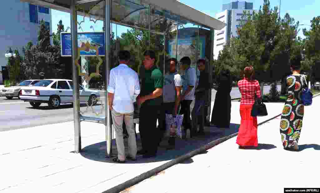 Aşgabadyň awtobus duralgalarynyň birinde günden goranmak üçin kölegede duran adamlar.