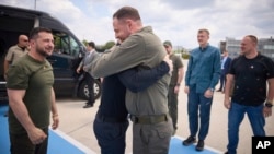 Ukrainian President Volodymyr Zelenskiy (left) smiles as the head of the Ukraine's presidential office, Andriy Yermak (center), hugs a defender of Mariupol's Azovstal steelworks before departing Istanbul international airport on July 8. 