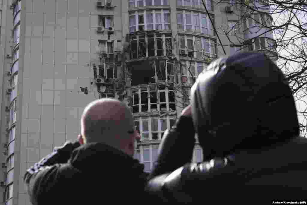 People look up at an apartment building damaged by a drone that was shot down during a Russian overnight strike on Kyiv.