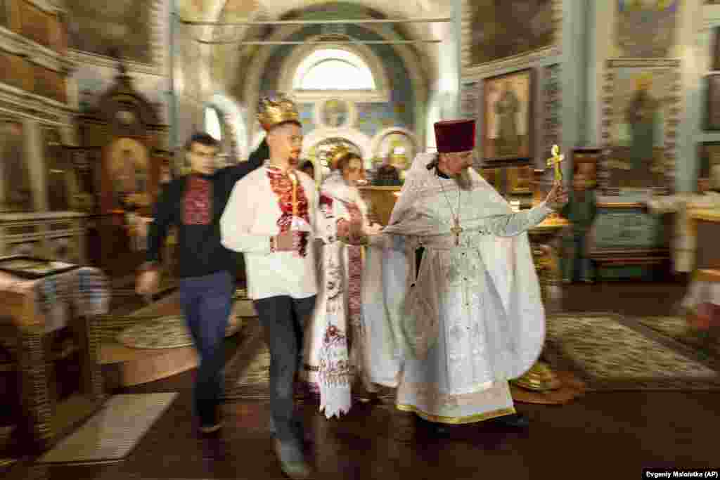 Украинский военнослужащий &laquo;Карп&raquo; и его невеста Анна идут рядом со священником во время церемонии венчания в Харьковской области, 24 июля. Рост числа свадеб в Украине в военное время напоминает ситуацию в разгар Второй мировой войны, но на другом конце света. В 1942 году в Соединенных Штатах было заключено 1,8 миллиона браков, и это был рекорд для страны