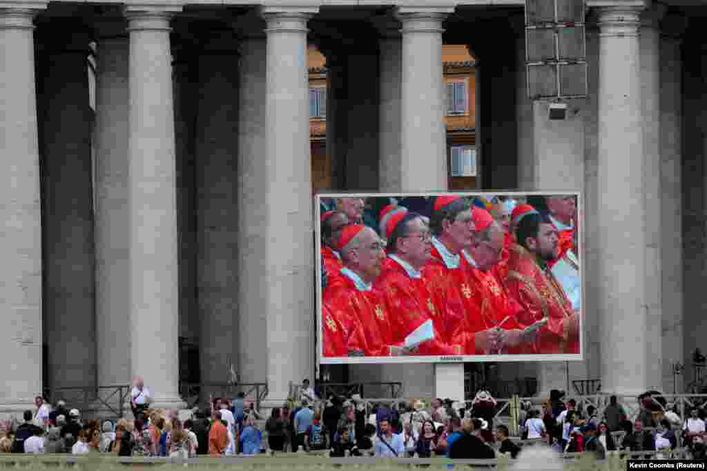 Люди дивляться святу месу на великому екрані на площі Святого Петра у Ватикані в перший день конклаву з обрання наступного папи, 7 травня 2025 року.Між кардиналами, які обиратимуть нового папу – Микола Бичок, кардинал УГКЦ (на екрані – праворуч)