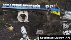 Украиналык аскерлер Орусиянын желегинин элеси түшүрүлгөн “Купянский район” деген жазууну бузуп, Украинанын байрагын көтөрүп турушат. Харьков облусу, 14-сентябрь, 2022-жыл. Казак сайты ушул Харьковдогу окуялар тууралуу жазган макаласы үчүн сотко чакырылууда.