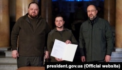 Президент України Володимир Зеленський (посередині) під час підписання заявки на членство України в Євросоюзі. Поряд із ним голова Верховної Ради Руслан Стефанчук (ліворуч) і прем'єр-міністр України Денис Шмигаль (праворуч). Київ, 28 лютого 2022 року. Швидкість, з якою Україна стала кандидатом в ЄС, вражає багатьох оглядачів