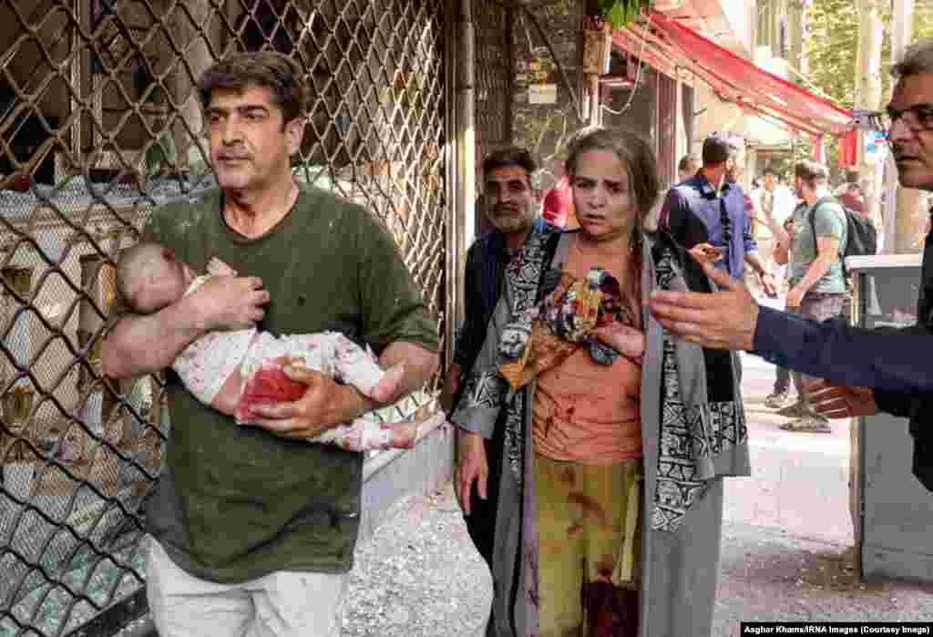 Мужчына нясе дзіця пасля выбуху ў Тэгеране, Іран, 15 чэрвеня 2025 году.