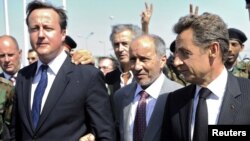Fransiýanyň prezidenti Nikolas Sarkozi we Britaniýanyň premýer-ministri Deýwid Kameron Liwiýanyň Milli Geçiş Geňeşiniň başlygy Abdel Jelil bilen bilelikde ýerli medisina merkezine sapar edýarler. Tripoli. 15-nji sentýabr, 2011.