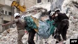 Суриянинг “Оқ дубулғалар” кўнгиллилар гуруҳи ҳукуматнинг Ариҳа шаҳрига ҳаво ҳужуми уюштиргани хабар қилингандан сўнг харобалар орасидан чиқариб олган жасадни кўтариб кетмоқда. Ариҳа “Amnesty”нинг ҳисоботида келтирилган жойлардин биридир. (Озодлик архивидан)