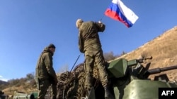 Two soldiers attaching a flag on the Russian peacekeeping forces' military vehicle as they move on the road towards Martuni in Nagorno-Karabakh. November 13, 2020.