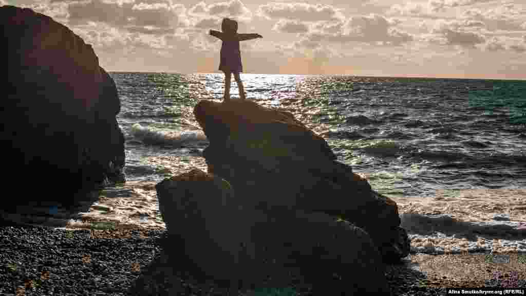 Дівчинка стоїть на верхівці валуна, що на пляжі в Судаку