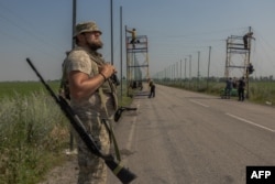 Український солдат чатує поки його товариші натягують сітку проти дронів над дорогою у Донецькій області. Липень 2025 року