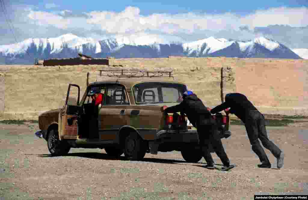 Сүрөттө: Кишилер Ыраң-Көл айылынын көчөсүндө эски машинаны түртүп баратышат. Экономикалык оор абалда, энергетикалык кризистин кучагында калган, кийинки кездери тил маселесинен чайналган мургабдык кыргыздар тарыхый мекенинeн колдоо жок, өз арбайын өздөрү согушууда.