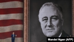 Президент США Дональд Трамп выступает на церемонии по случаю 75-й годовщины высадки союзных войск в Нормандии 5 июня 2019 года на фоне флага США и портрета президента времен Второй мировой Франклина Д. Рузвельта