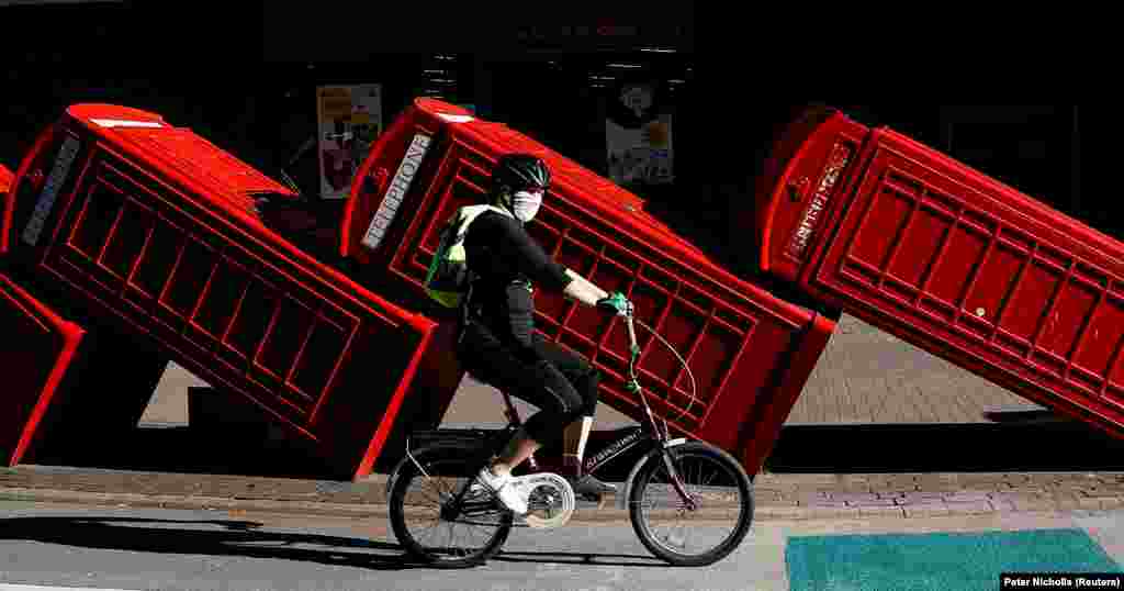 Велосипедист їде в захисній масці повз інсталяцію &laquo;Out of Order&raquo; скульптора Девіда Мача. Дванадцять червоних телефонних будок класичної моделі, які є настільки ж упізнаваним символом Великої Британії, як і поштові скриньки та двоповерхові автобуси, покладені на бік за &laquo;принципом доміно&raquo;