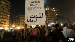 Тахрир аянтындагы демонстранттардын бири түрдүү тилдерде жазылган "Баасыз өлүм" деген ураанды кармап турат. Каир, 2-июнь 2012