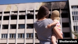Мама з дитиною біля будівлі в Маріуполі, зруйнованого внаслідок бойових дій у 2014 році. Фото: 19 липня 2015 року