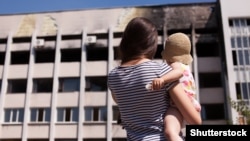 Мама с ребенком у здания в Мариуполе, поврежденного в результате обстрела, 19 июля 2015 года