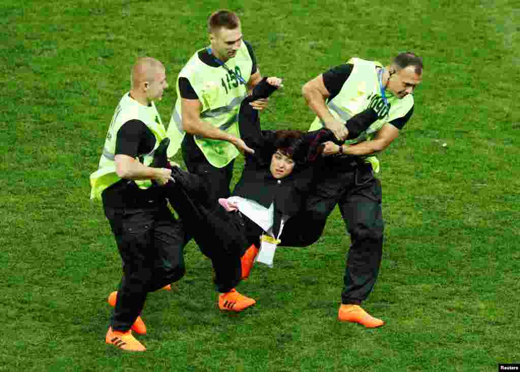 A woman being hauled off the pitch by stewards.&nbsp;