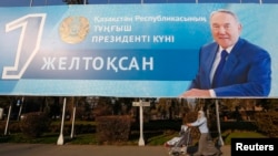 Женщина с ребенком проходит под баннером с изображением Нурсултана Назарбаева, установленным перед Днем первого президента Казахстана. Алматы, 30 ноября 2015 года