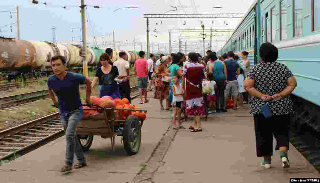 Парень с нагруженной арбузами и дынями тележкой предлагает пассажирам купить бахчевые.