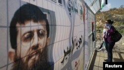 Кадер Аднандын сүрөтү түшүрүлгөн баннердин жанында турган демонстрант.  2012-жыл, февраль. Палестина. 