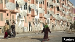 Женщины идут в Туркменабате рядом с жилым домом, на стенах которого установлены спутниковые антенны.