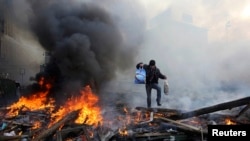 Ukraine -- A man walks amidst burning remains of fires at Independence square in Kyiv, February 21, 2014