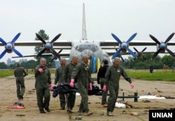 Офіцери українських військово-повітряних сил несуть тіло людини, яка загинула в результаті падіння винищувача