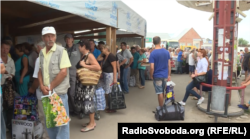Люди з торбами стоять у черзі, щоб перетнути лінію розмежування