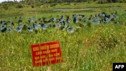 Предупреждающий знак с надписью "Район, загрязненный диоксином. Посевы, выпас скота и птицы и рыболовство запрещены". Окрестности озера Хо Сен рядом с аэропортом города Дананг во Вьетнаме