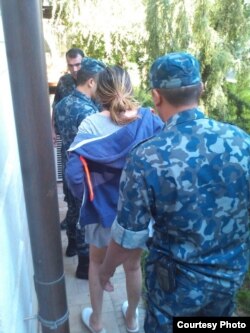 Гулнора Каримова бир гуруҳ ҳарбий кийимдаги эркакларнинг қаттиқ назорати остида қолаётганини тушуниш мумкин.