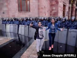 Passersby take selfies in front of riot police guarding the government building in Yerevan's Republic Square on the evening of April 19.
