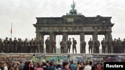 ГДРдин чек арачылары Бранденбург дарбазасынын алдындагы Берлин дубалынын үстүндө тизилип турушат. 11-ноябрь 1989