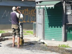 Бездомний чоловік чепуриться біля колонки