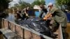 Volunteers and municipal workers place bags containing bodies retrieved on June 16 from flooded houses in a vehicle after floodwaters receded following the breaching of the Kakhovka dam.