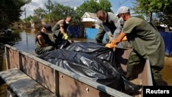 Volunteers and municipal workers place bags containing bodies retrieved on June 16 from flooded houses in a vehicle after floodwaters receded following the breaching of the Kakhovka dam.