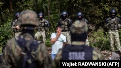 Адзін зь мігрантаў, як мяркуецца, з Афганістану, стаіць, спрабуючы падаць заяву аб міжнароднай абароне ў Польшчы, недалёка ад мяжы зь Беларусьсю. 20 жніўня 2021 году