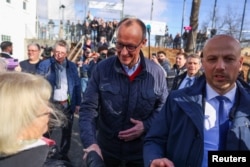 Friedrich Merz, liderul blocului conservator Uniunea Creștin-Democrată (CDU) - Uniunea Creștin-Socială (CSU), candidat pentru funcția de cancelar, dă mâna cu o femeie înainte de a-și exprima votul, în Arnsberg, 23 februarie 2025.