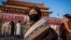 Tourists from Tibet wearing a protective mask (R) and a scarf as a mask (C) walk in front of the portrait of late communist leader Mao Zedong (back) at Tiananmen Gate in Beijing on January 23, 2020. - China is halting public transport and closing highway 