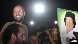 Ливия лидери Муаммар Каддафинин уулу Сайф ал-Ислам Триполиде  атасынын портрети менен жактоочулары жана журналисттердин ортосунда турат.  23-август.