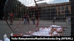 Хлопці та дівчата, одягнуті в біле, лежать на асфальті під «закривавленим» котком з металевих ґрат